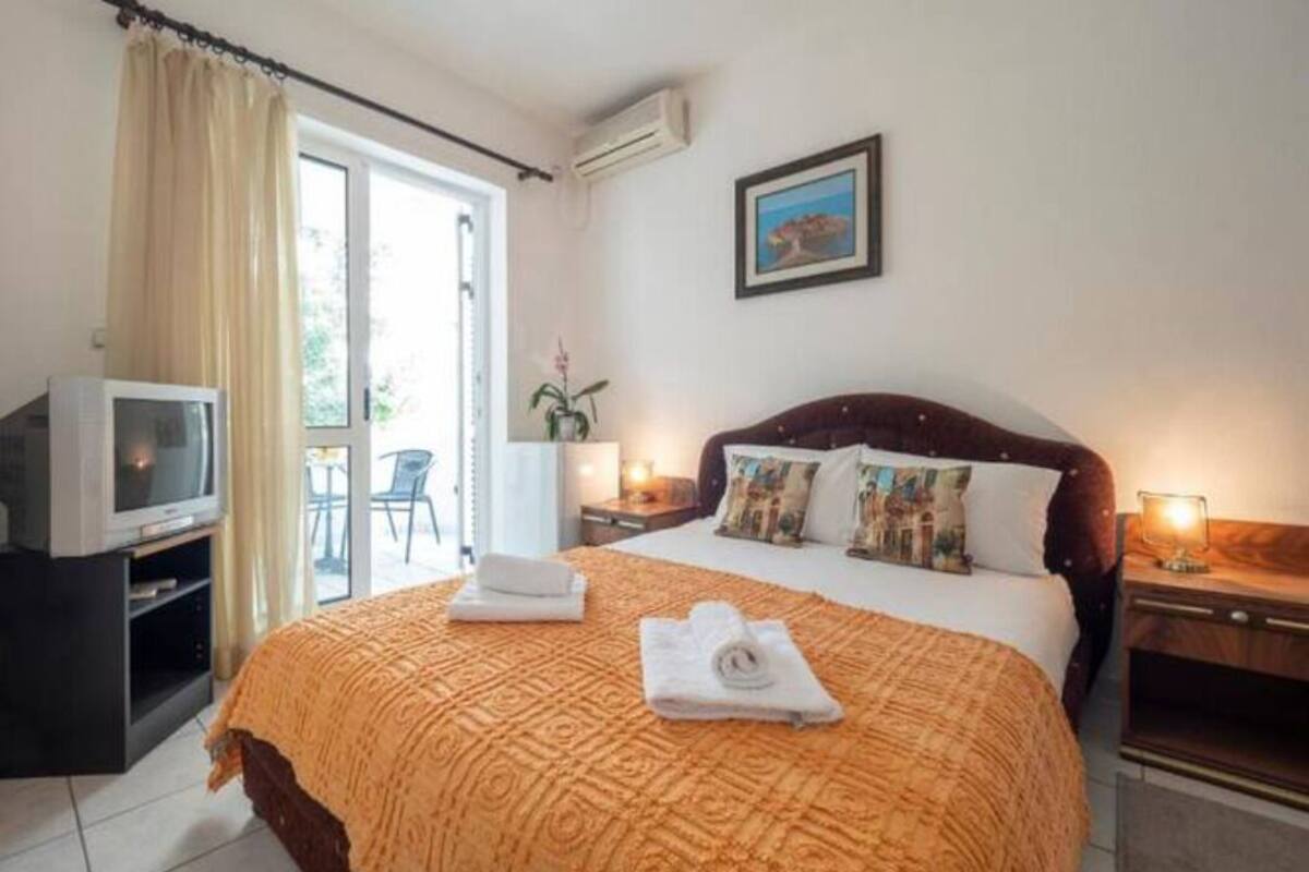 A hotel room with a large bed, a television, a desk, and a balcony with curtains.