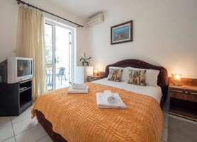 Ein Hotelzimmer mit einem großen Bett, einem Fernseher, einem Schreibtisch und einem Balkon mit Vorhängen.