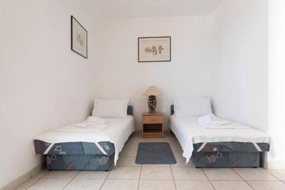A small, clean room with two beds, a nightstand, a lamp, and a framed picture on the wall.
