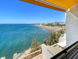 Une vue sur la côte depuis un balcon, avec un ciel dégagé, une plage et des bâtiments visibles au loin.