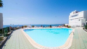 A swimming pool with a clear blue sky and a view of the sea in the background. - Ocean Front Apartment (Maspalomas)