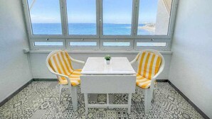 A corner room with a view of the sea through large windows, two striped chairs, a small table, and patterned floor tiles. - Ocean Front Apartment (Maspalomas)