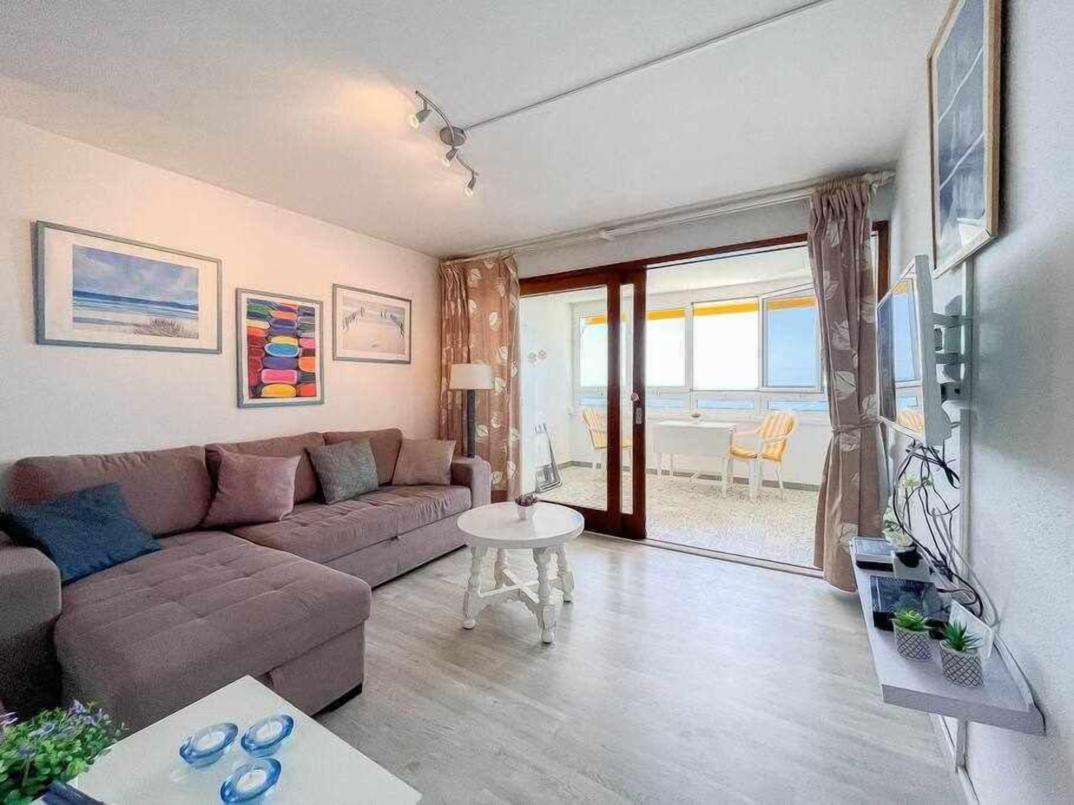 A modern living room with a sofa, a small round table, and a balcony with chairs.