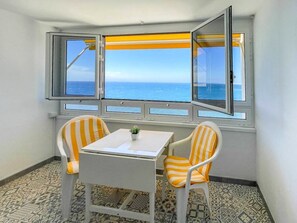 Une chambre d’angle avec vue sur la mer, deux chaises à rayures, une petite table et des carreaux de sol à motifs.