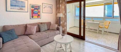 A living room with a sofa, a small round table, and a view of the balcony.