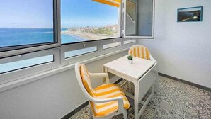 A room with a view of the ocean, a table with two striped chairs, and a small plant on the table. - Ocean Front Apartment (Maspalomas)