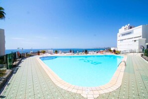Une piscine avec un ciel bleu azur et une vue sur la mer en arrière-plan.