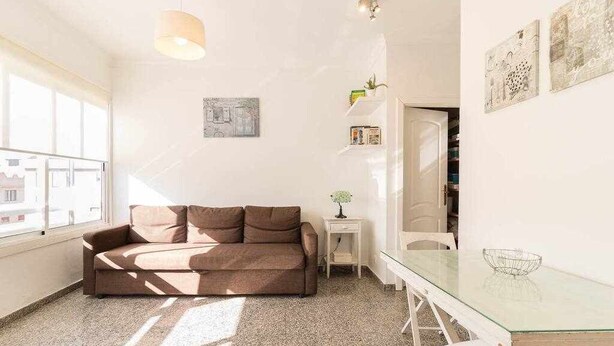 Ein modernes Wohnzimmer mit einem braunen Sofa, einem Glastisch und einem kleinen Beistelltisch mit einer Vase.