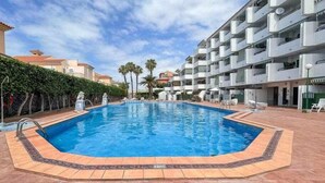 Ein rechteckiger Swimmingpool mit einer gefliesten Umrandung, umgeben von einer gefliesten Terrasse.