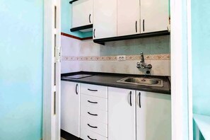 A compact kitchen with white cabinets, a black countertop, and a stainless steel sink.