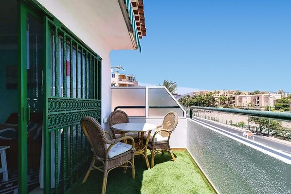 A balcony with a table and chairs, a green railing, and a view of the cityscape.