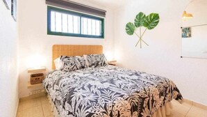 Ein Schlafzimmer mit einem Bett, einem Fenster, einer wandmontierten Pflanze und einem Nachttisch mit einer Lampe.