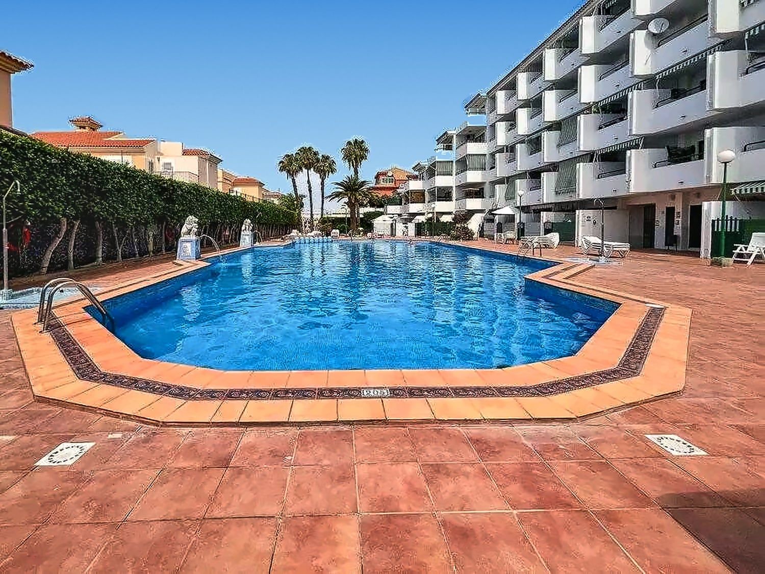 Une piscine bordée de carreaux, entourée d’une terrasse également carrelée.