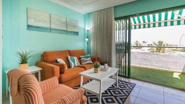Ein Zimmer mit Türkiswänden, einem gestreiften Sofa, einem weißen Couchtisch und Blick auf einen Parkplatz durch eine Glastür.