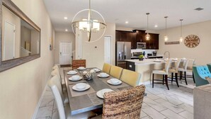 Una cocina moderna con armarios oscuros, una isla central y una zona de comedor con una mesa grande dispuesta para seis comensales.