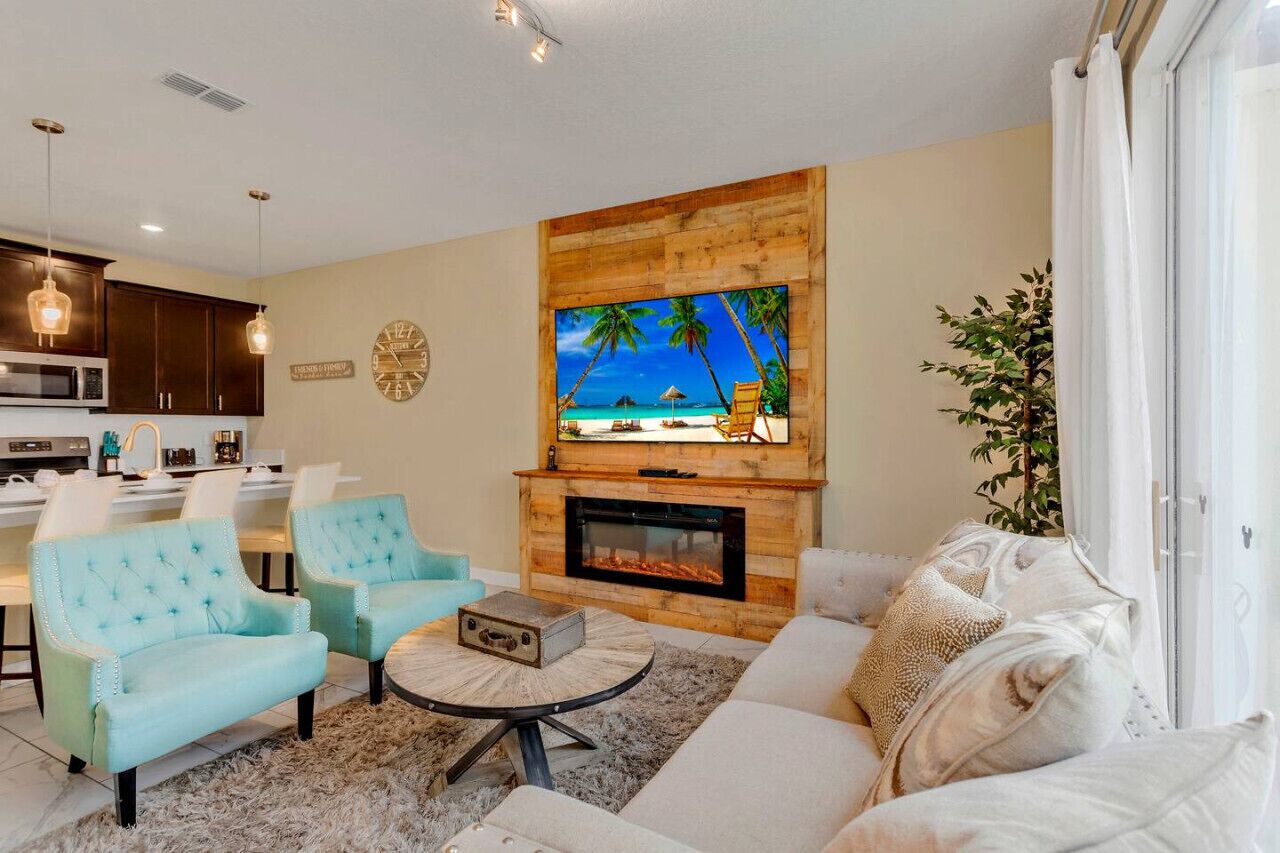 Una sala de estar con chimenea, un televisor montado encima y un comedor con sillas y una mesa.