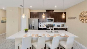 Una cocina moderna con armarios oscuros, electrodomésticos de acero inoxidable e iluminación colgante.