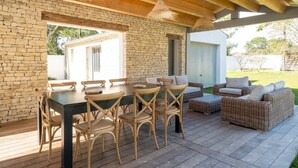 Un espace extérieur abrité, aménagé pour les repas, avec un mur en pierre, un plafond en bois, des meubles en osier et une vue sur le jardin.