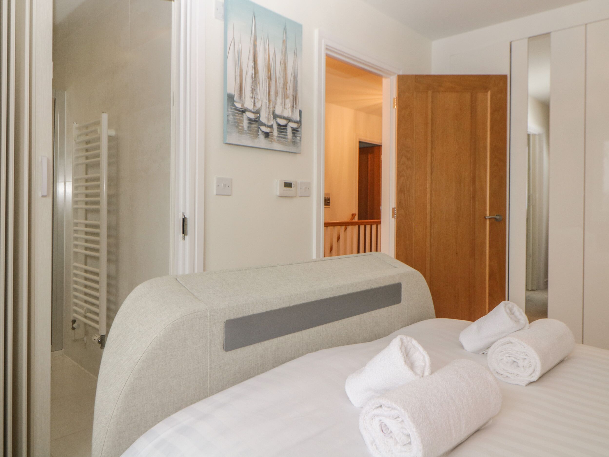 A hotel room with a bed, a painting of sailboats on the wall, a wooden door, and a white towel on the bed.