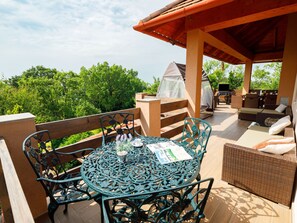 Une terrasse extérieure couverte, avec une table ronde et des chaises, un canapé en osier et un espace barbecue.