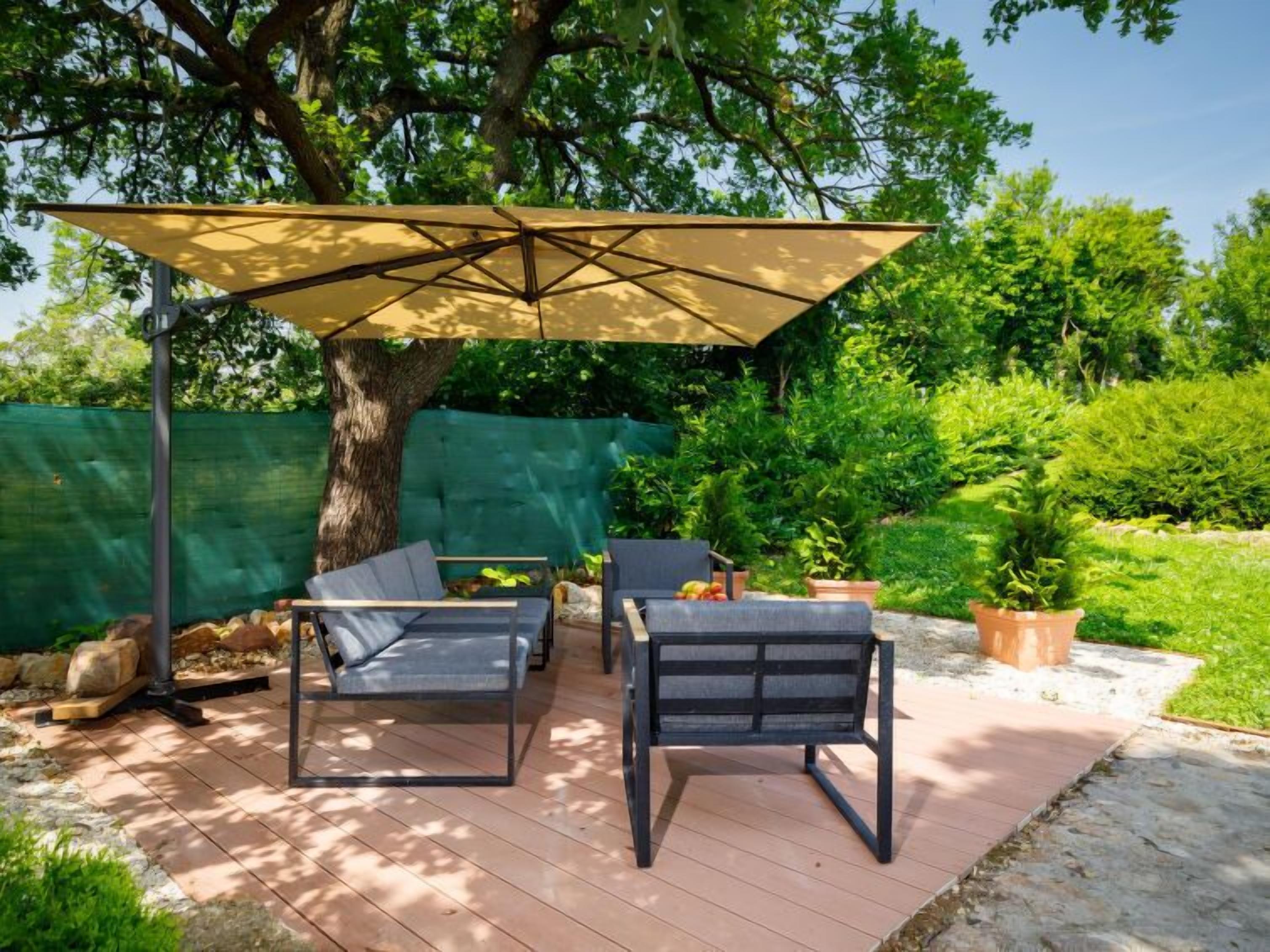 An outdoor patio with two lounge chairs and a table, shaded by a large umbrella.