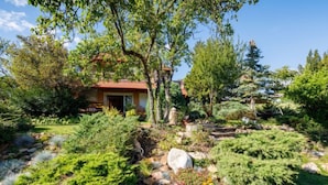 A landscaped garden with a variety of plants and a stone pathway leading to a building with a red roof.