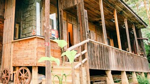 A rustic wooden cabin with a porch, large windows, and a stone wall. - Wine Space (Ambrolauri)