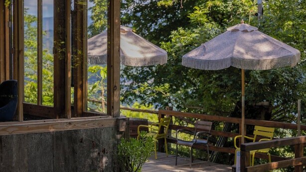 A wooden deck with two thatched umbrellas, wooden railings, and benches. - Wine Space (Ambrolauri)