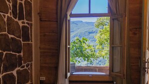 A bedroom with two beds, stone walls, a wooden ceiling, and a window with a view of greenery and hills. - Wine Space (Ambrolauri)