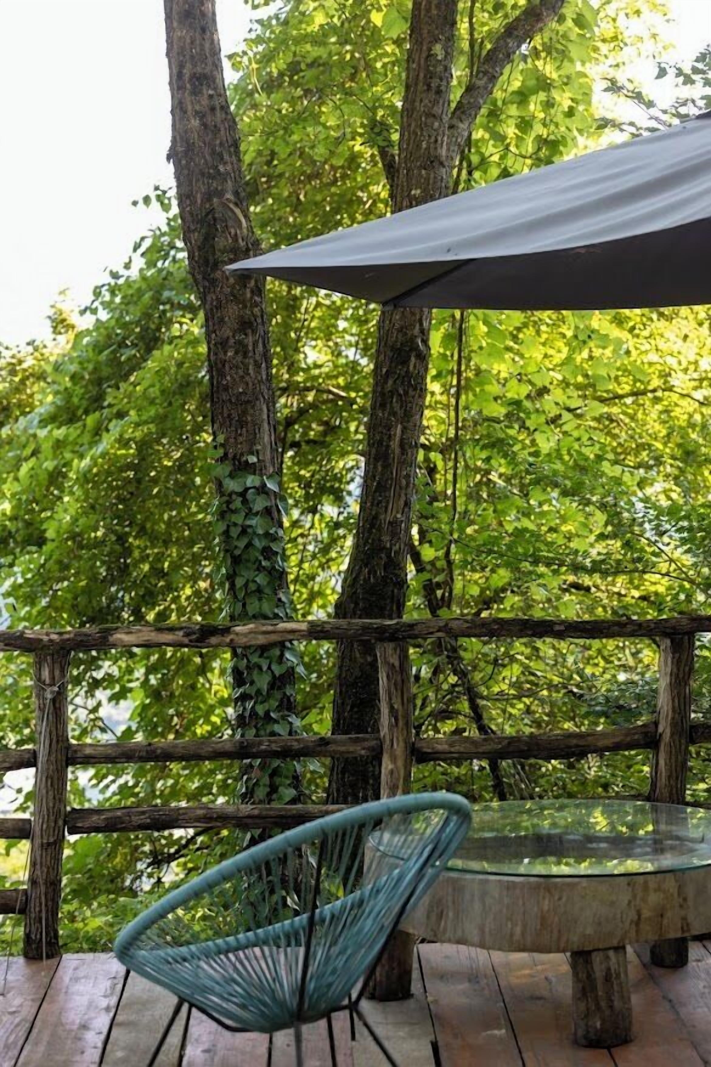 A wooden deck with a glass table and a blue chair, surrounded by trees.
