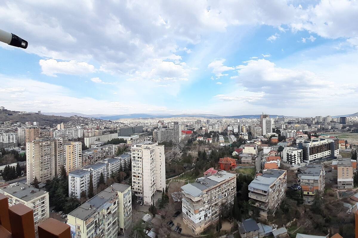A cityscape with high-rise buildings, a clear sky, and a balcony with a chair.