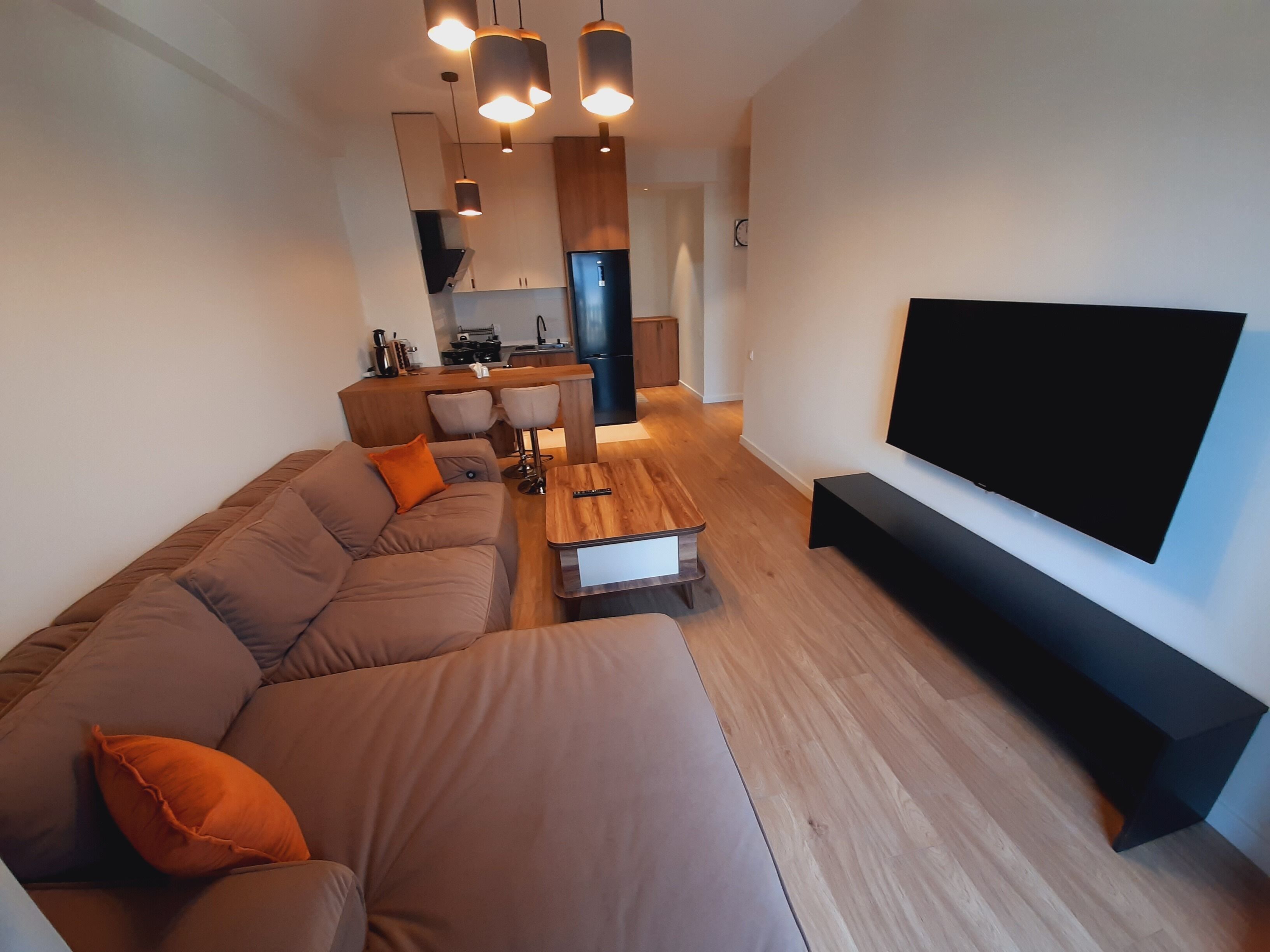 Un salon moderne avec un canapé d’angle, une table basse et un téléviseur à écran plat fixé au mur.