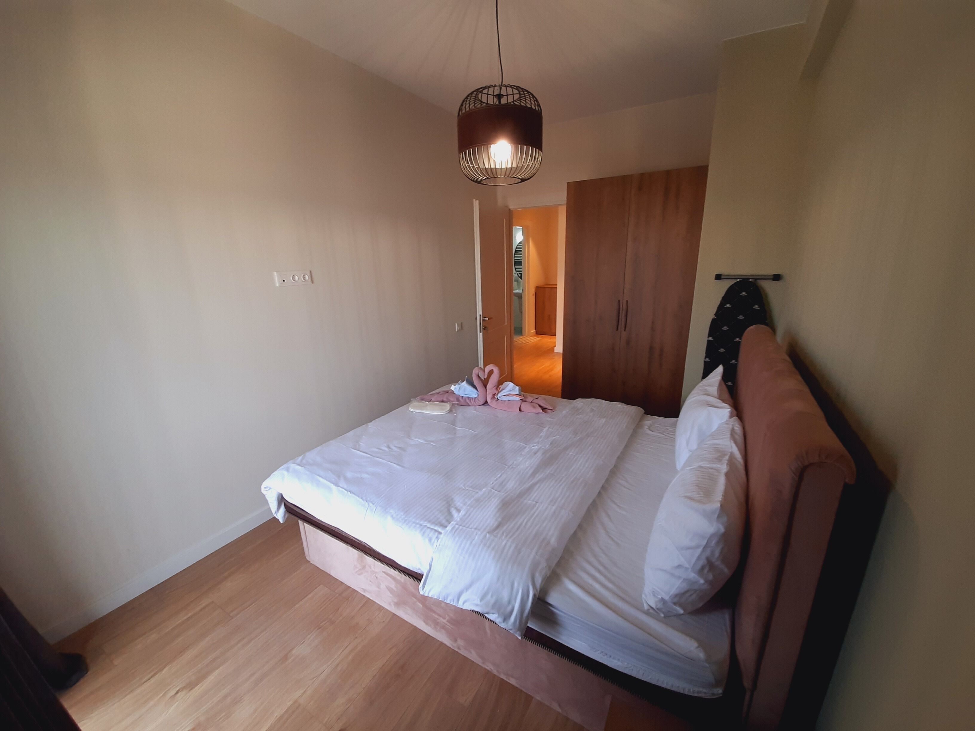 Un dormitorio con cama, suelo de madera, armario y lámpara colgante.