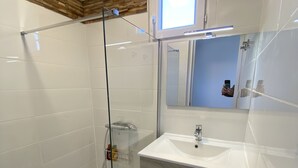 Un baño moderno con cabina de ducha de vidrio, un lavabo blanco y un mueble de tocador de madera.