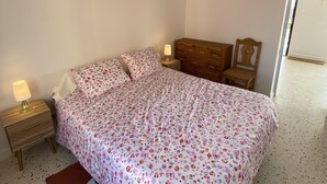 Un dormitorio con cama, mesita de noche, cómoda, lámpara colgante y un cartel en la pared.