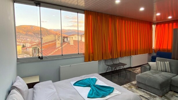 Una moderna camera d'hotel con un letto grande, un divano, un tavolo da pranzo e vista sulla città attraverso ampie finestre.