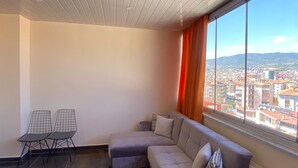 Un soggiorno moderno con un divano componibile, un tavolino con sedie e un'ampia finestra vista città.
