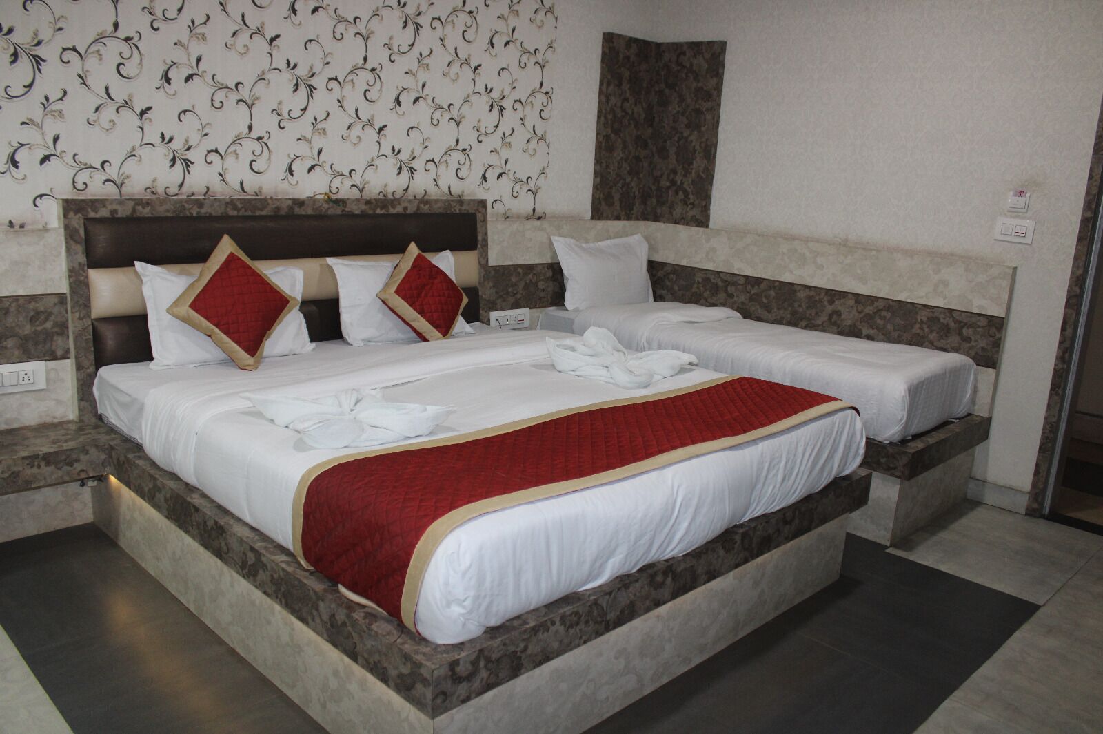 Una cama doble con cubrecama rojo y blanco, dos almohadas y un cojín decorativo rojo.