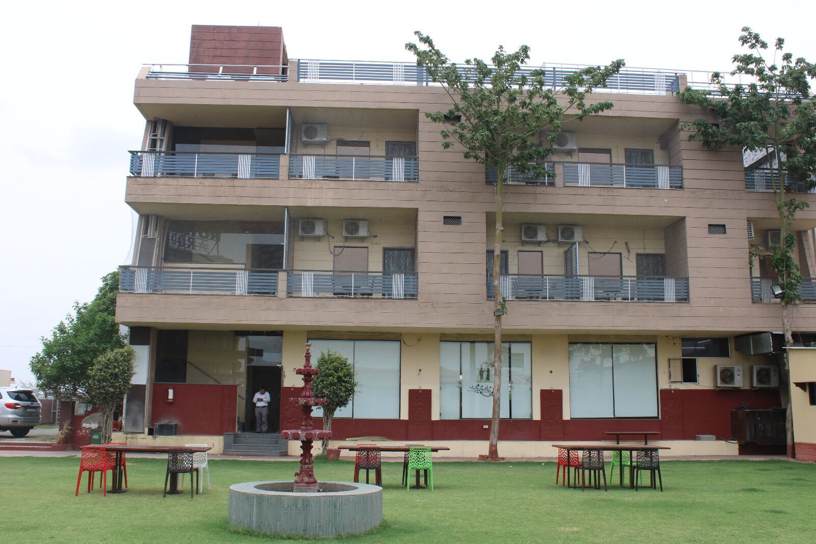 Un edificio de varios pisos con balcones, unidades de aire acondicionado y un pequeño jardín con mesas y sillas.