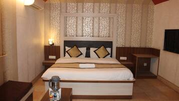 A hotel room with a large bed, two bedside tables, a nightstand, a wall-mounted air conditioner, and a small table with a remote control and a glass.