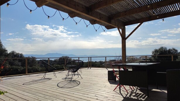 Eine Holzterrasse mit einer Pergola, Sitzmöbeln im Freien und Blick auf das Meer.