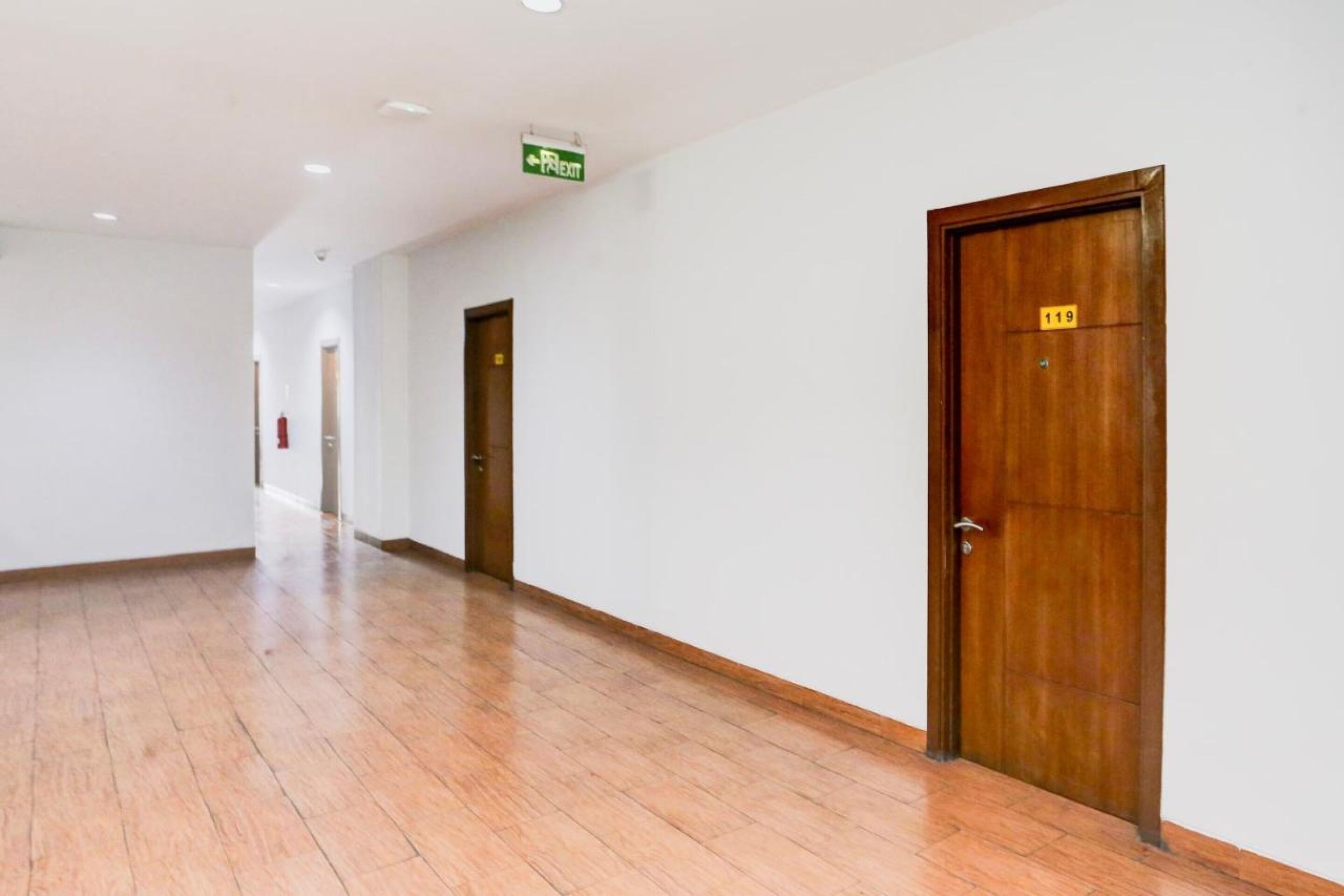 A hallway with wooden flooring and doors, one marked with the number 119.