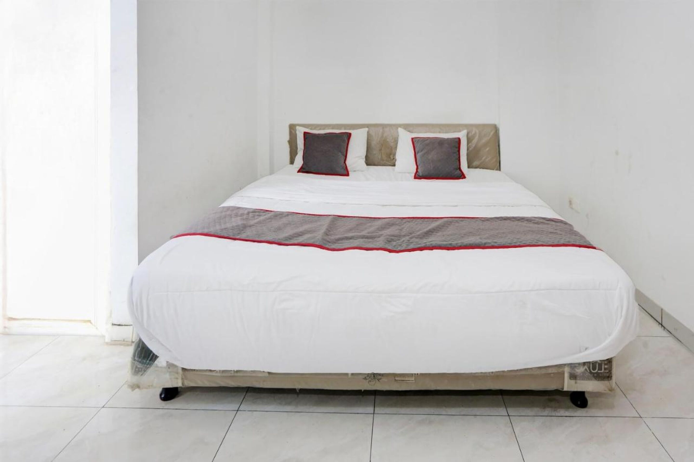 Cama com colchão branco, almofadas de destaque cinza e vermelhas, e manta cinza.
