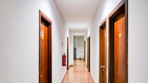 Un pasillo de hotel con puertas de madera, un extintor y un accesorio de iluminación en el techo.