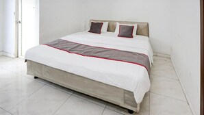 Una cama bien hecha con una colcha blanca y gris, dos almohadas y un cabecero de madera.