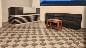 A room with a checkered floor, a black leather sofa, a small wooden table, and a reception desk with a towel hanging on it. - Hotel Ocean View Vizag (Visakhapatnam)