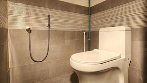 A bathroom with a toilet, a shower, and a green hose. - Hotel Ocean View Vizag (Visakhapatnam)
