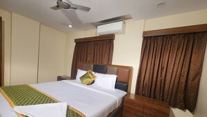 A hotel room with two beds, a ceiling fan, an air conditioning unit, wooden headboards, and a wooden nightstand with a phone. - Hotel Ocean View Vizag (Visakhapatnam)