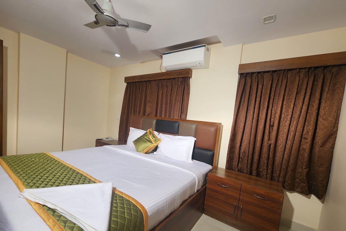 Une chambre d’hôtel avec deux lits, un ventilateur de plafond, un appareil de climatisation, des têtes de lit en bois et une table de chevet en bois avec un téléphone.