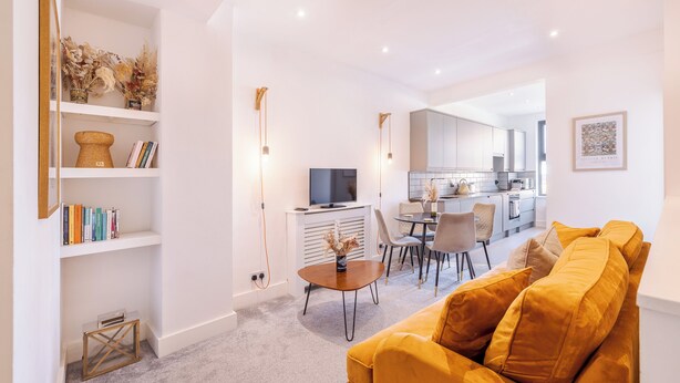 Een moderne woonkamer met een bank, een salontafel en een televisie. Achtergrond is een keuken met een eethoek.